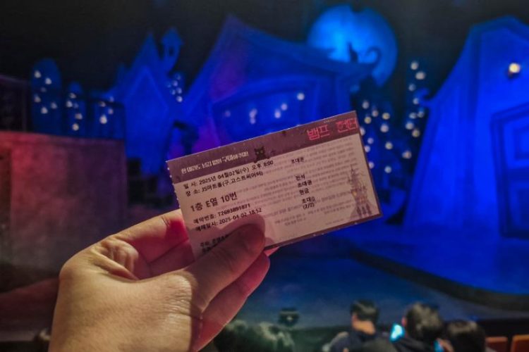 close up of hand holding a ticket in front of a blue-lit stage