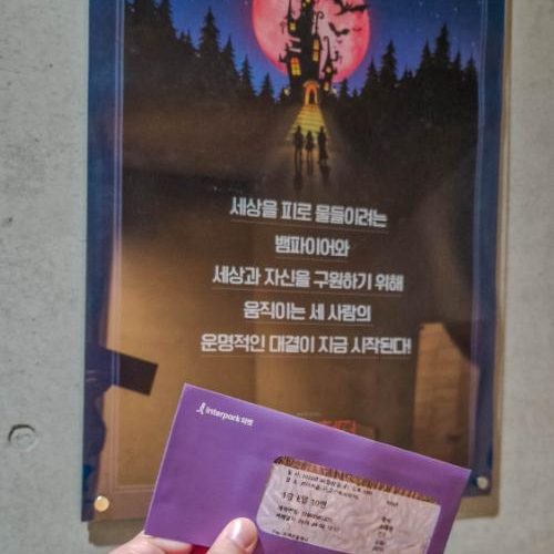 holding up an envelope with a ticket in front of musical poster