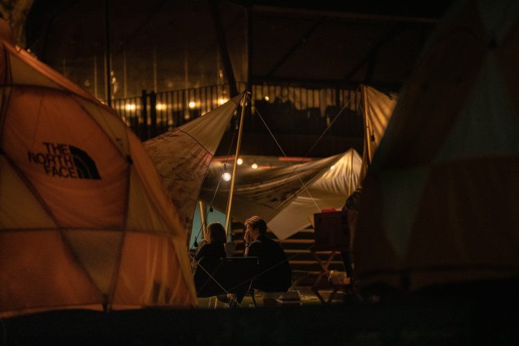 two people sitting among lit tents at night