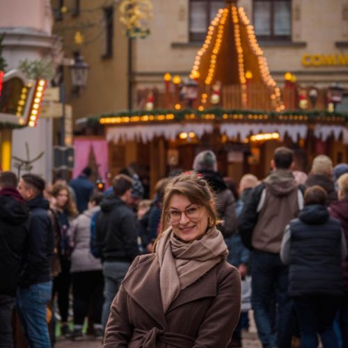 woman in brown coat stands in front of Christmas market pyramid