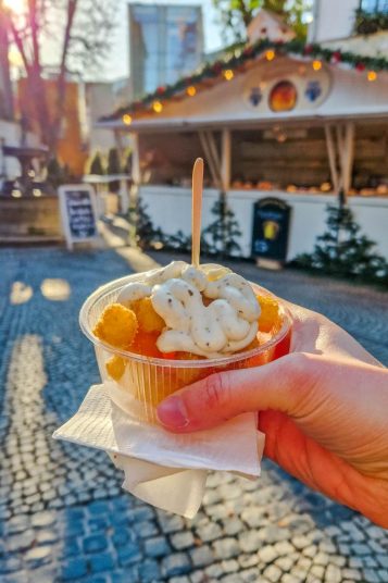 hand showing a small cup full of potato bites with cream on top
